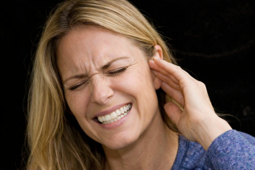 Kvinde omkring 40 år med lyst hår holder sig for øret og oplever tinnitus med ringen eller susen i øret.