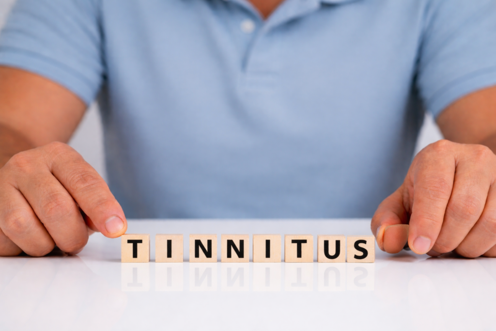 Hånd placerer bogstaver, der danner ordet “tinnitus”, som symbol på en vedvarende lydoplevelse i nervesystemet.